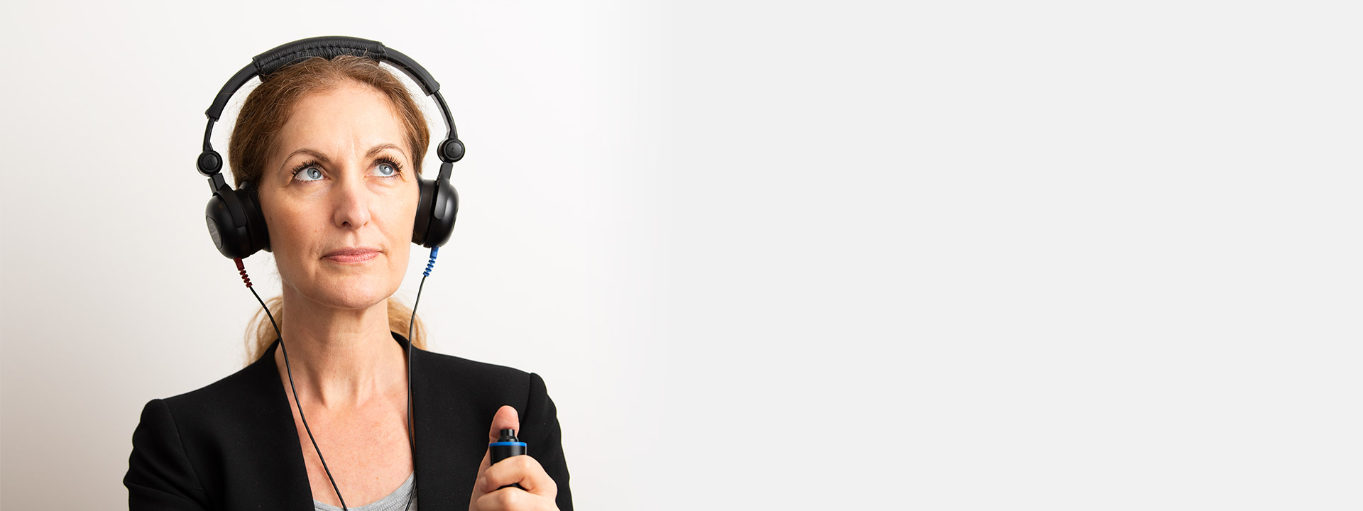 Woman undergoing a hearing test, wearing headphones and holding a response button.