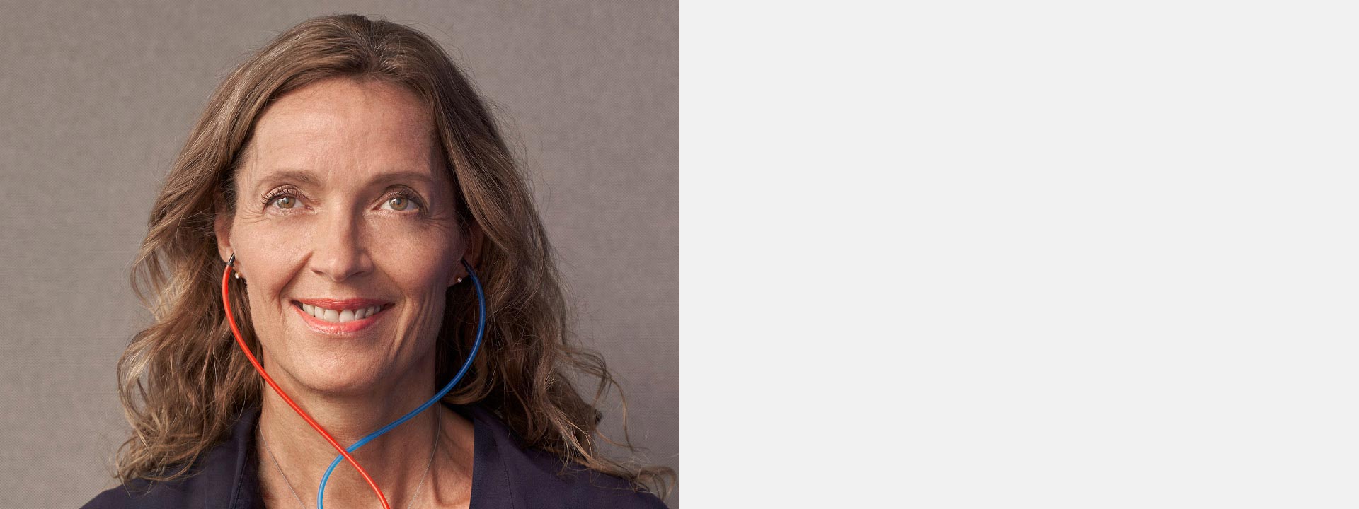 Woman smiling during a hearing test with red and blue wired earphones.