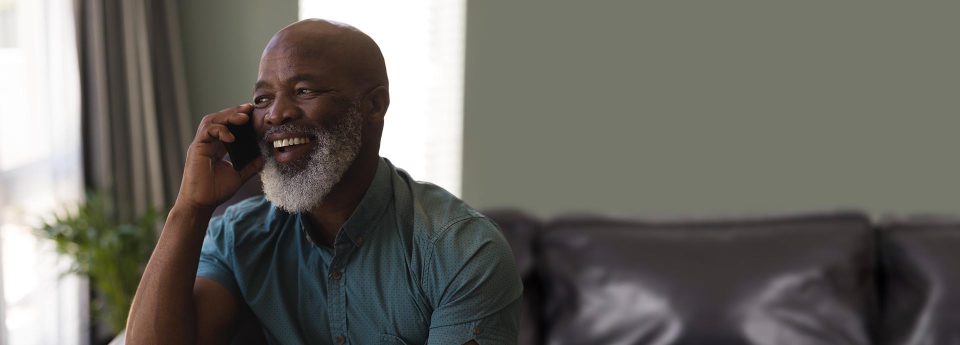 Man wearing a hearing aid and smiling while talking on the phone indoors.