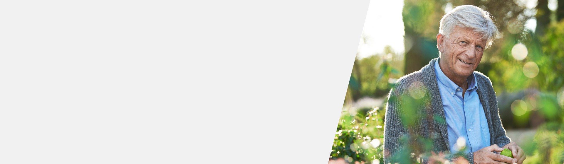 Man with hearing loss smiling in a sunny garden surrounded by plants.