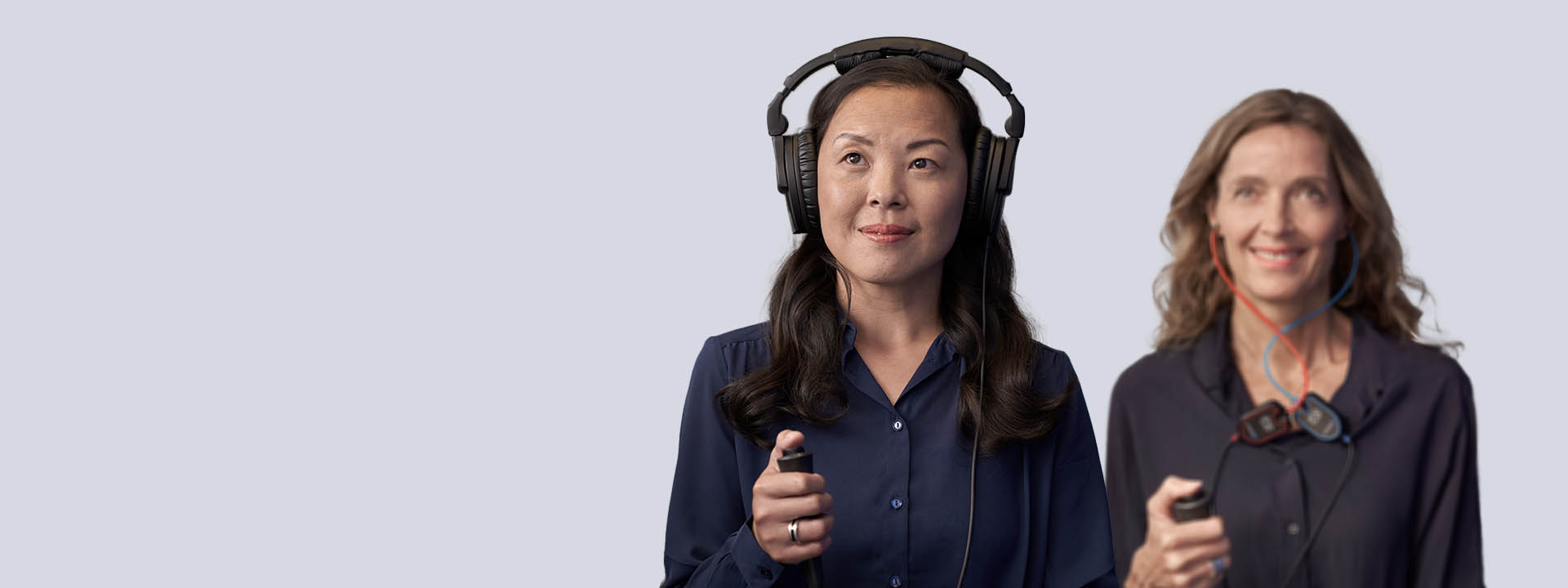 Two women participating in a hearing assessment using headphones and handheld response devices.