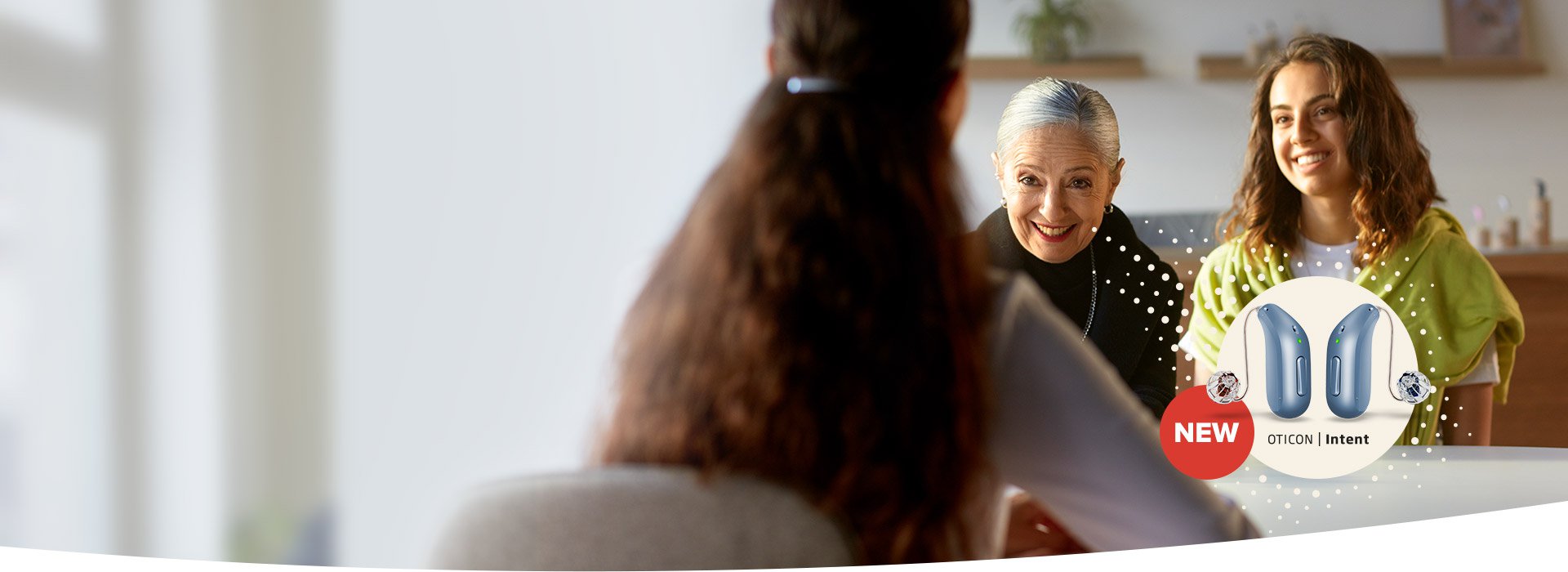 Elderly woman and younger woman sharing a smile in a warm home environment, highlighting the features of Oticon's new hearing aids.