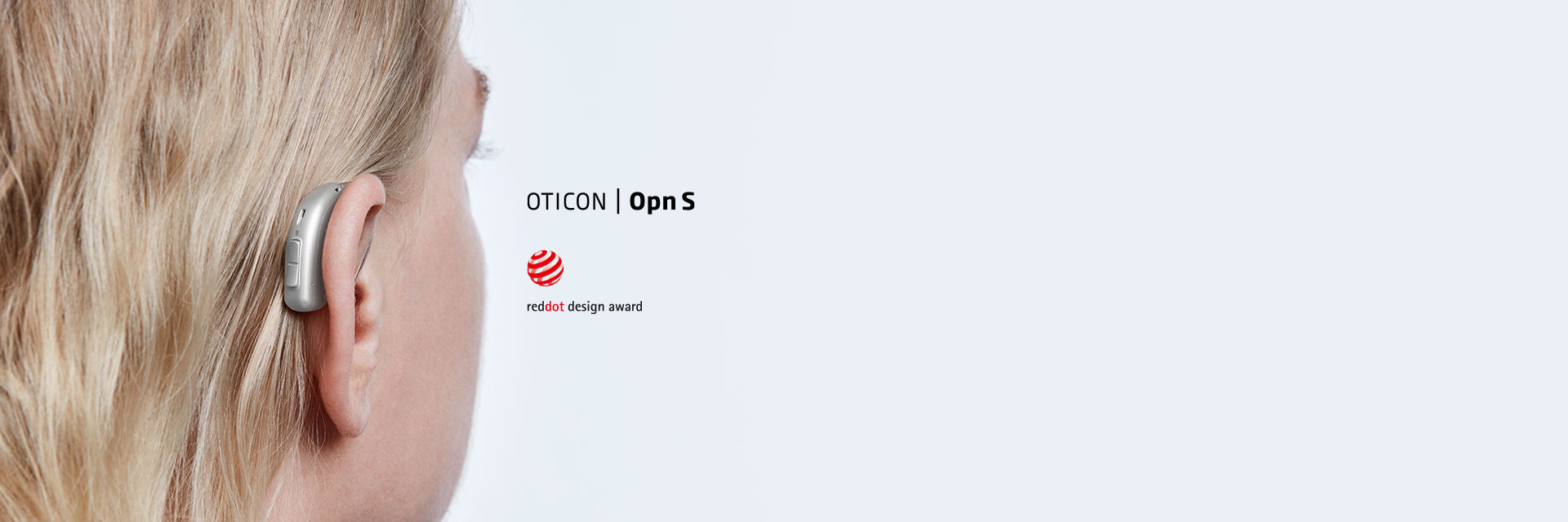 A sleek Oticon Opn S hearing aid rests discreetly behind a person’s ear amidst blonde hair. The text reads: ’OTICON | Opn S’ and ’reddot design award’ with the award logo.