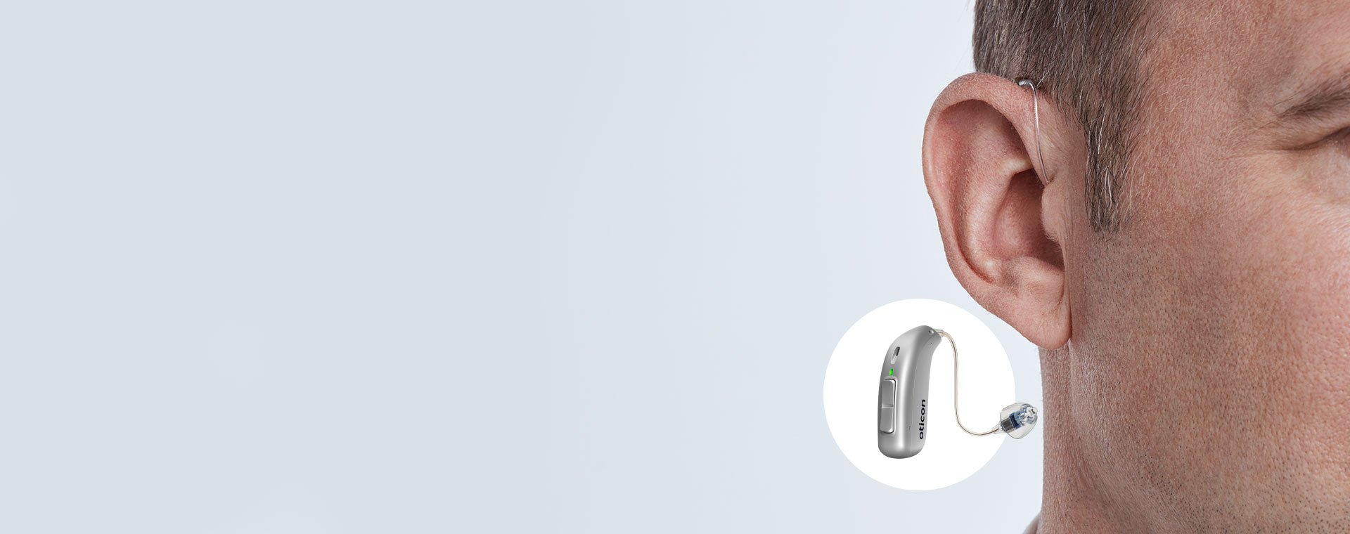 Hearing aid positioned behind the ear of a man, showcasing the Oticon hearing device design.