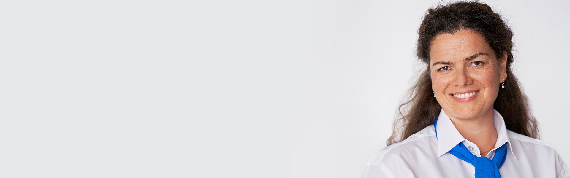 Smiling woman wearing a white shirt and blue scarf, representing professional hearing care services.