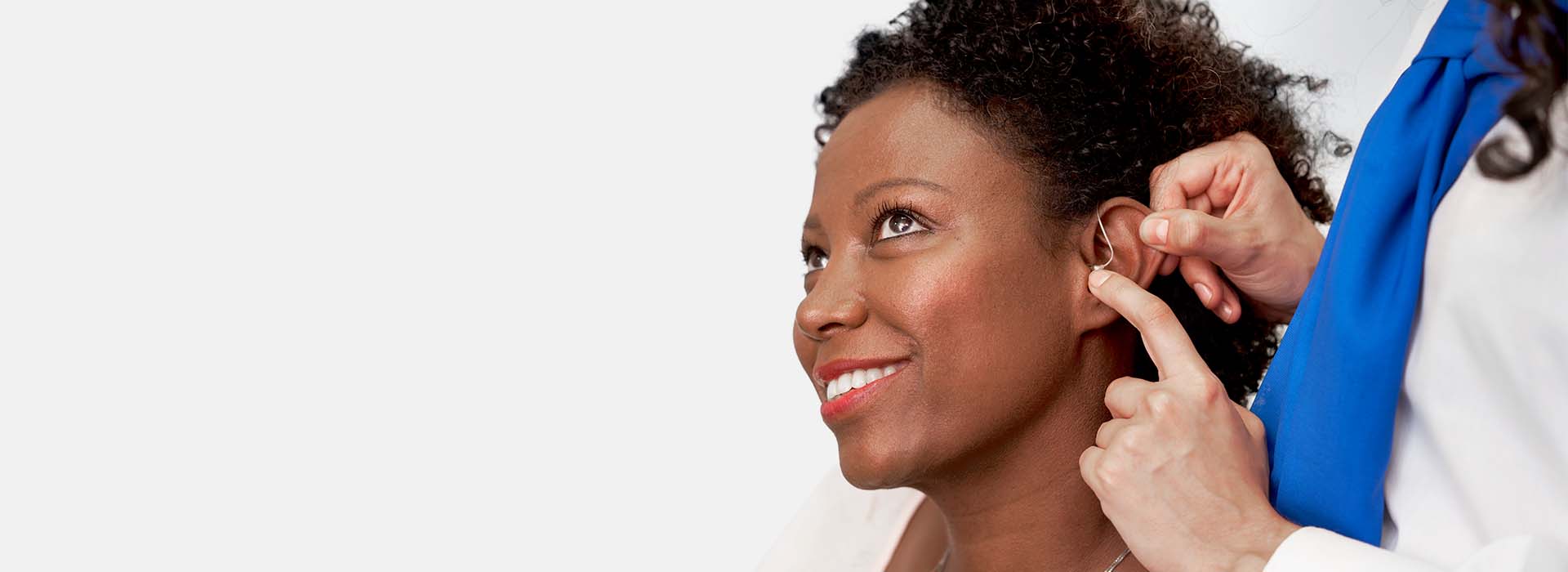 Audiologist fitting a hearing aid into a woman's ear.
