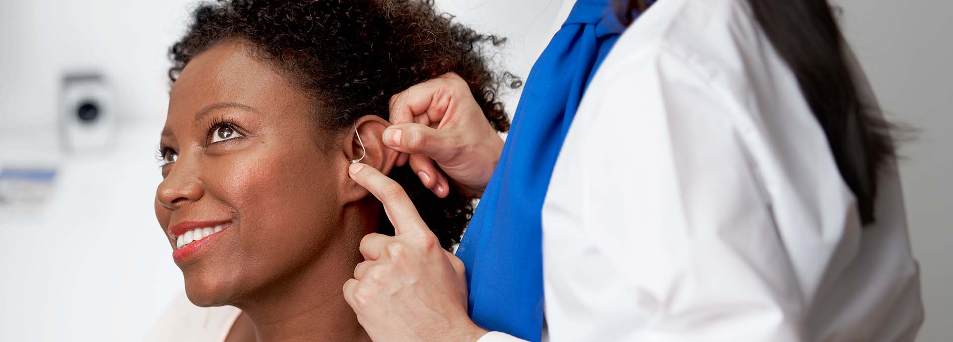 Woman receiving assistance with fitting a hearing aid behind her ear.