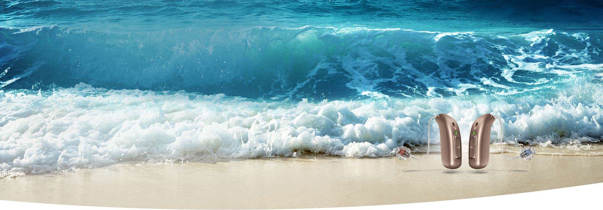 Two sleek hearing aids rest on a sandy beach, with ocean waves crashing in the vibrant blue background, emphasizing clear sound and a connection to nature. No identifiable brand is visible.
