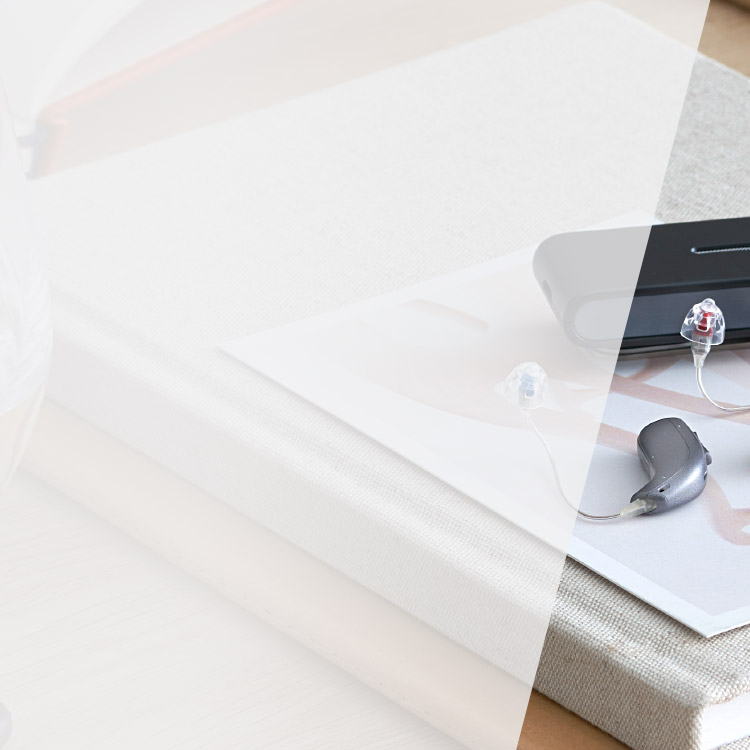 A sleek hearing aid with transparent tubing rests on a document near a device case, placed atop a fabric-bound book on a table.