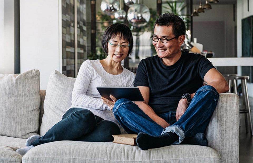 Couple smiling and engaging with a tablet on a comfortable sofa in a stylish, modern living room.