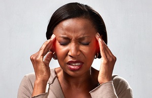 Woman with closed eyes pressing her temples with both hands, possibly experiencing discomfort, stress, or a headache, against a neutral grey background.