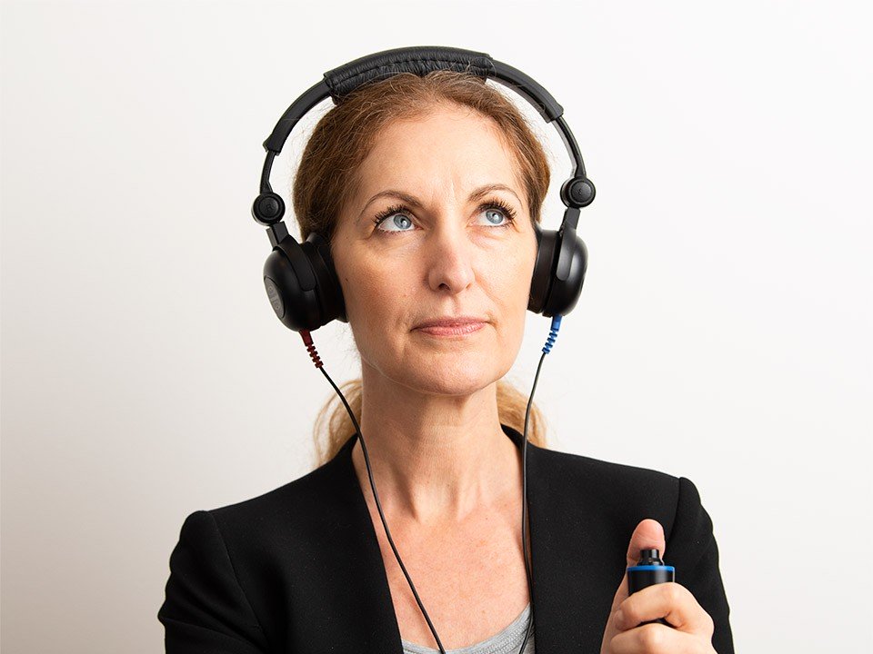 Woman wearing headphones and holding a button during a hearing test.