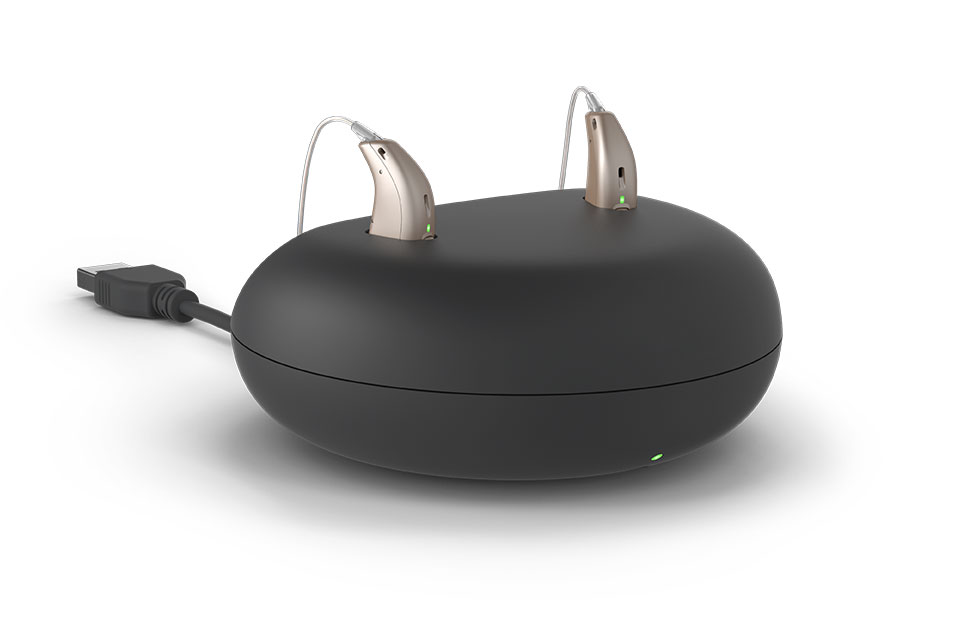 Rechargeable hearing aids placed in a black charging case connected via USB cable.
