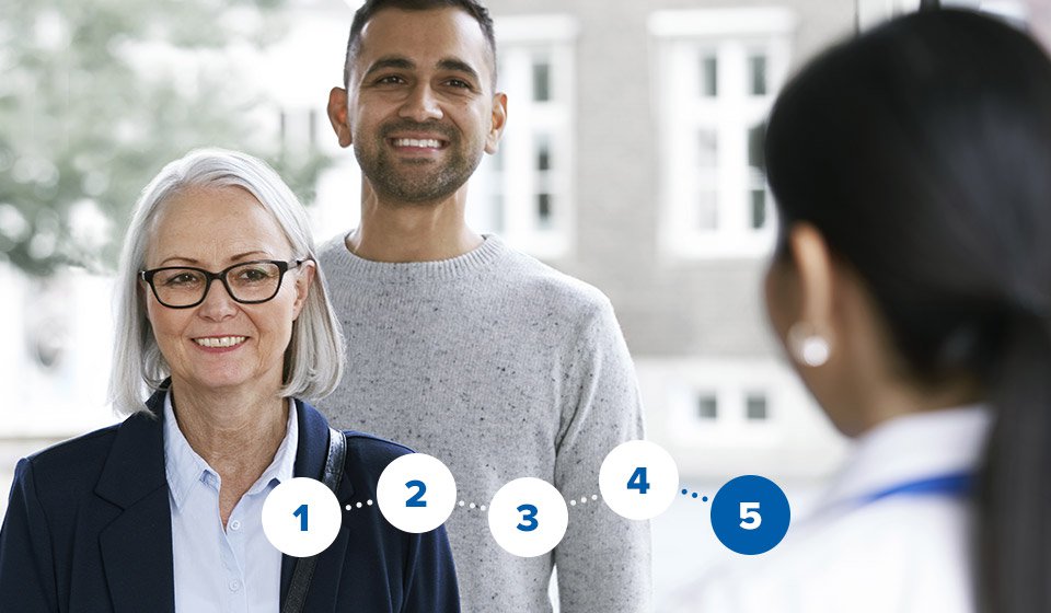 Audiologist greeting man and woman at a hearing clinic reception.