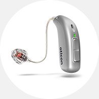 A silver hearing aid equipped with a small wire and earbud rests against a white background. The device has a button, a green light, and the brand name "oticon" written on it.