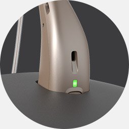 Close-up of a hearing aid placed in a charger with a green indicator light.
