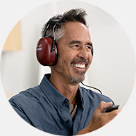 A person wearing red over-ear headphones undergoes a hearing test, holding a response button in a professional hearing clinic setting. The context suggests audiological assessment services like those offered by HearingLife.