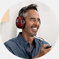 A man wearing red over-ear headphones taking a hearing test, holding a response button in a hearing clinic.