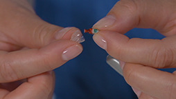 Fingers carefully hold a small, colorful hearing aid, contrasted against a soft blue background.