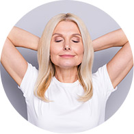 Smiling woman with blonde hair posing confidently, hands resting behind her head.