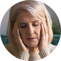 A woman with closed eyes rests her head in her hands, appearing stressed or contemplative, indoors with a green sofa in the background.