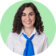 A person wearing a white shirt with a blue tie stands against a solid light green background. Their face is intentionally blurred to maintain privacy. No text or identifiable hearing aid brands are visible.