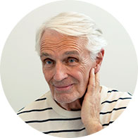 Elderly person with white hair holding hand to their ear.