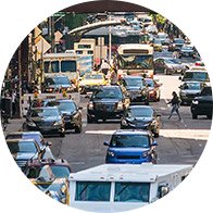 Busy city street with heavy traffic, including cars, buses, and pedestrians crossing.