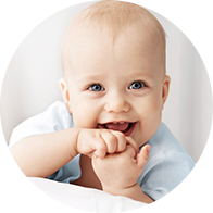 Smiling baby with hands near mouth in soft lighting.