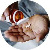 Hand holding a pill while pouring from a medication bottle.