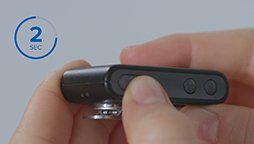 Hands holding a small, black, rectangular device with buttons being pressed, indicated by an overlay showing 