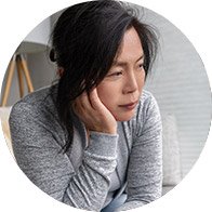 Woman sitting indoors with a hand on her chin, appearing contemplative and upset.