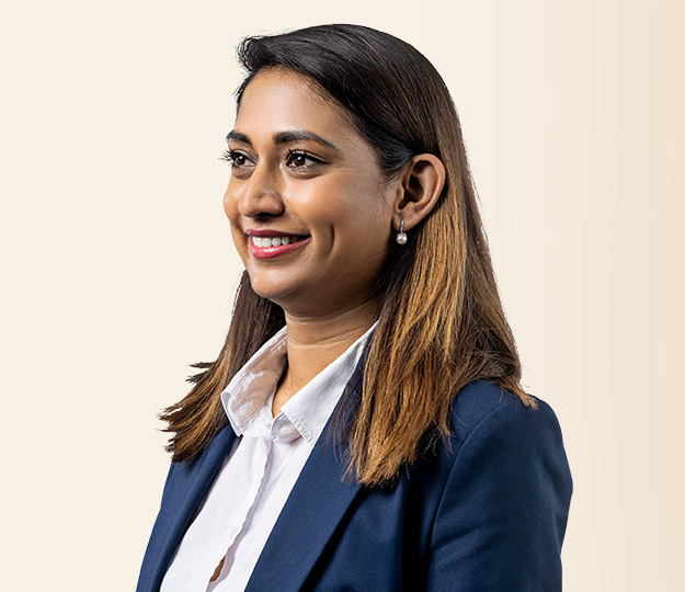 A professional woman wearing a navy blazer, white collared shirt, and pearl earrings smiles while facing slightly to the side. She is set against a plain beige background.