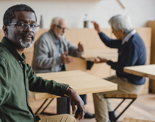 Man looking concerned at a cafe while two others are immersed in conversation.