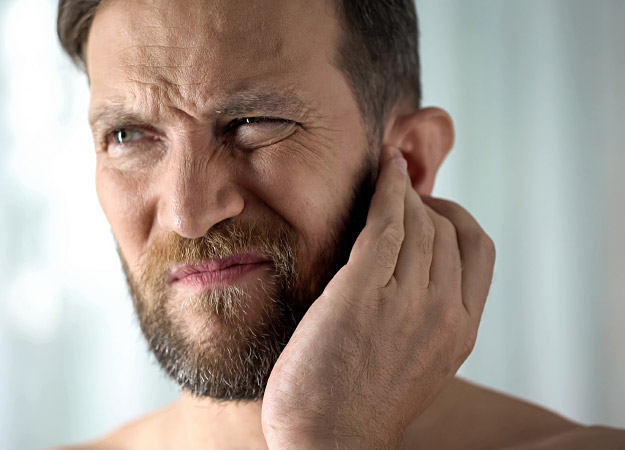 Man expressing discomfort while touching his ear, suggesting symptoms of tinnitus or hearing-related issues.