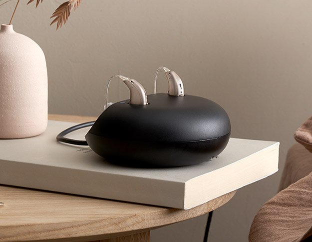 Rechargeable hearing aids resting on a sleek black charging case placed on a book near a minimalist decor setting.