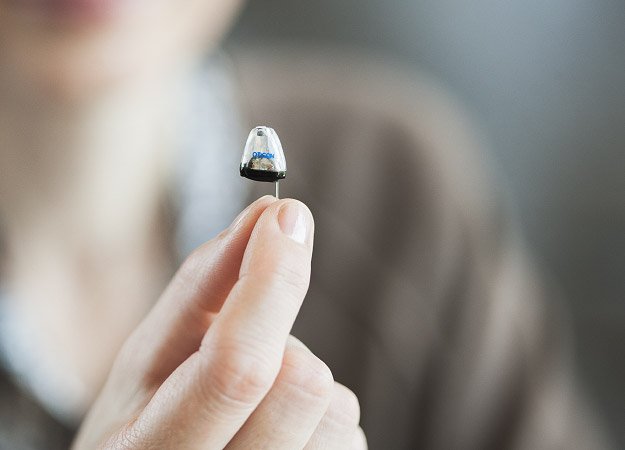 Hand holding a discreet, small hearing aid against a blurred background.