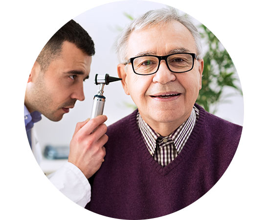 Audiologist conducting an ear examination on a smiling older man with age-related hearing difficulties.