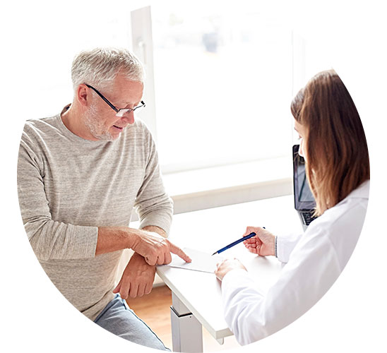An older man discusses paperwork with a doctor in a bright, modern office setting.