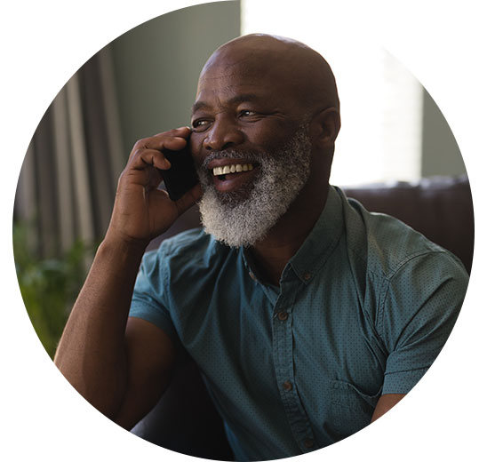 Man with a beard smiling while having a phone conversation indoors.