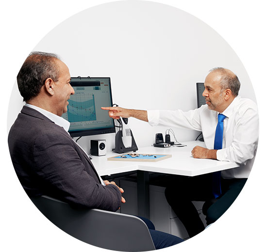 Man discussing hearing test results with audiologist as audiogram is displayed on computer screen.