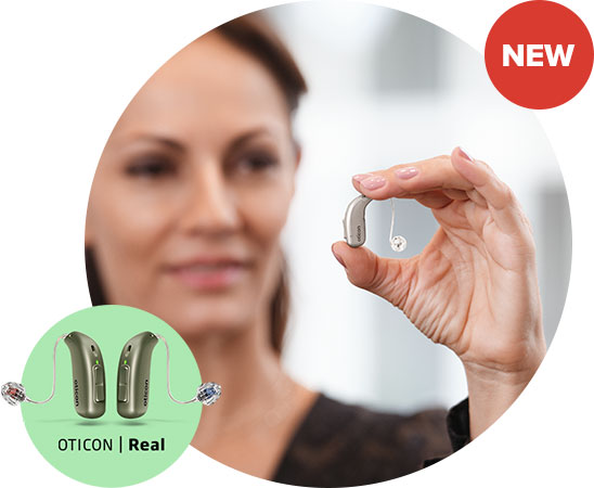 A hand holds an Oticon Real hearing aid, showcasing its compact design. A green overlay highlights two Oticon Real hearing aids with ’Oticon | Real’ text. A red ’NEW’ tag is displayed.