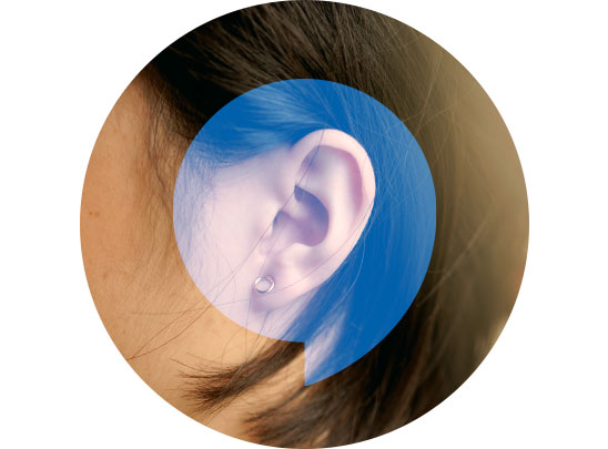 A discreet hearing aid rests behind a woman’s ear, framed by dark hair. The visual overlay includes HearingLife’s signature blue speech bubble design, emphasizing personalized hearing care services and solutions.