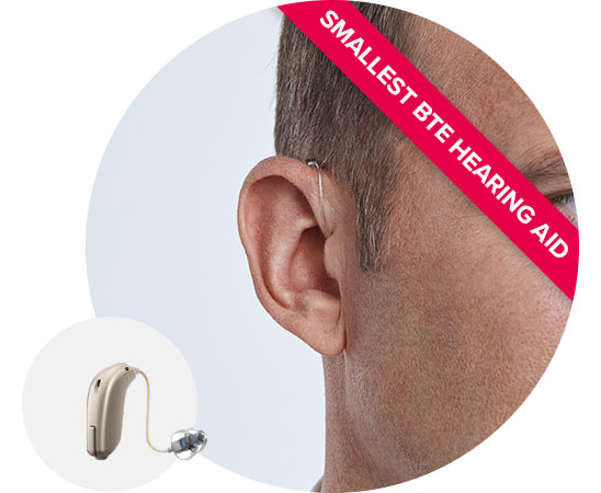 Man wearing a discreet receiver-in-the-ear hearing aid labeled as the smallest behind-the-ear (BTE) hearing aid.