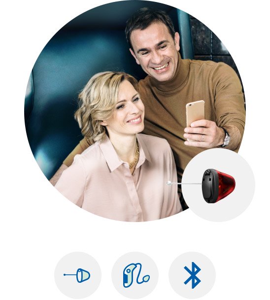 Man and woman smiling while using smartphones, with a discreet in-ear hearing aid highlighted.