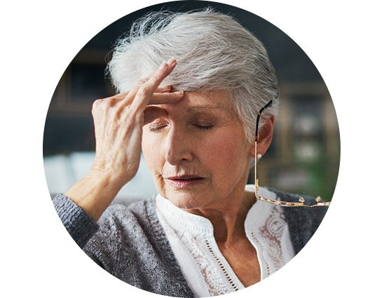 Woman with short gray hair holding her head and glasses, possibly indicating discomfort or frustration.