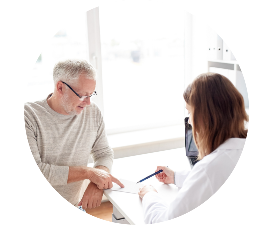 A man with glasses points at a document while a person in a white coat writes on it with a pen, in a bright office with large windows.