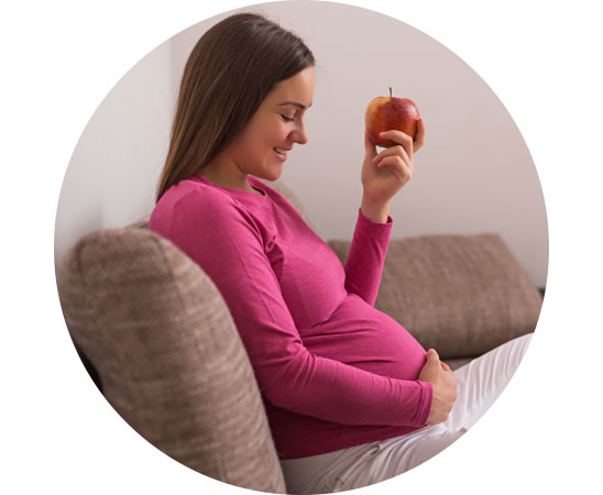 Pregnant woman sitting on a sofa holding an apple.