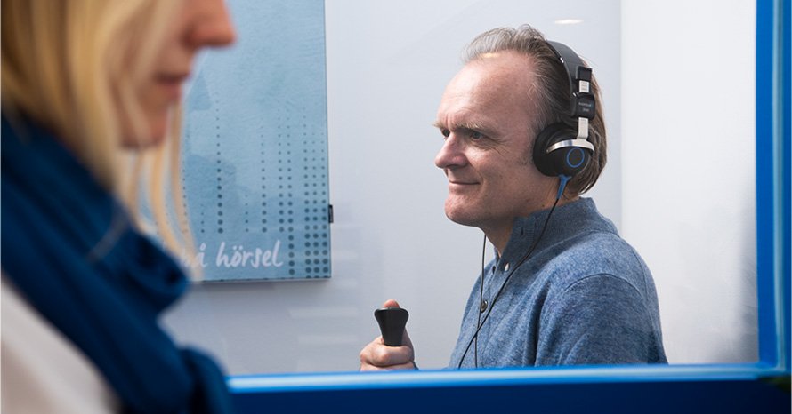 Un homme portant un casque audio passe un test auditif dans une cabine insonorisée.
