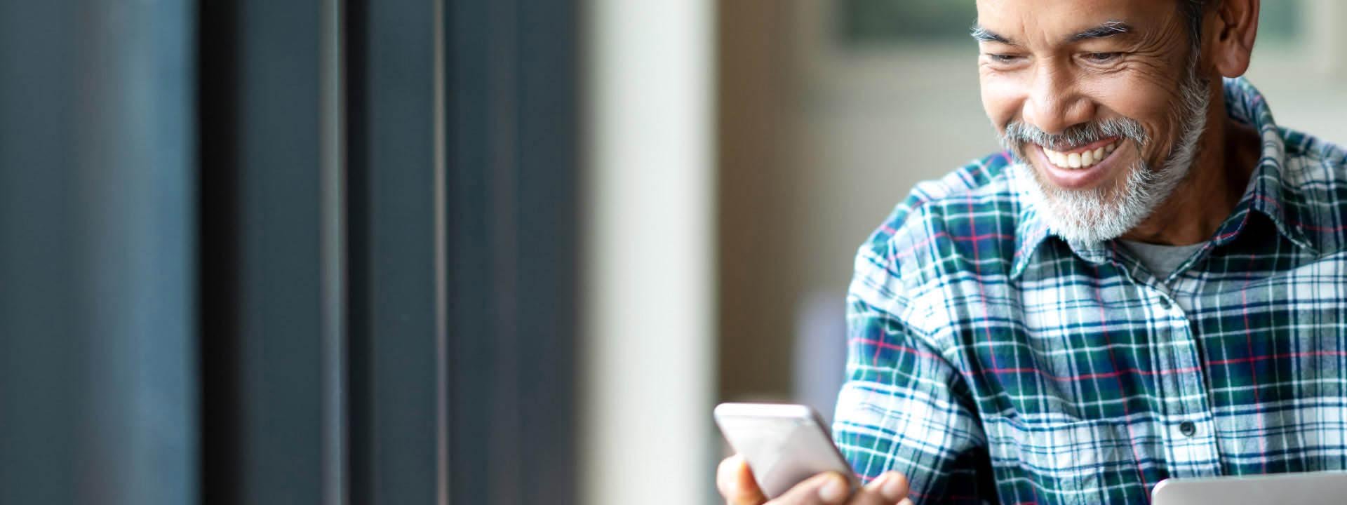 Un homme âgé consulte son téléphone portable près d’une fenêtre.
